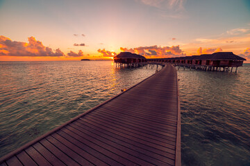 Amazing tropical sunset at Maldives. Luxury over water resort villas bungalows seascape with soft led lights under colorful sky. Exotic summer holiday or vacation sunset sunrise resort hotel seascape