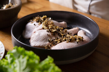 Raw chicken legs on a black plate marinated with garlic, pepper, meat with ingredients for cooking.