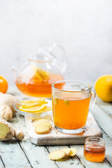 Ginger tea in a glass cup with lemon and mint on light background