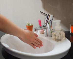 Light-skinned Asian woman rinsing hands in the bathroom sink. Shows hygiene and cleanliness for...