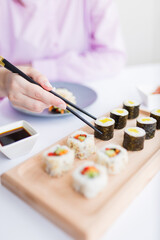 Woman hand taking piece of sushi roll with chopsticks. Healthy seafood asian japanese dish.