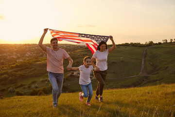 Cheerful family is having fun running along the grass in a summer park. USA July 4th Celebration.