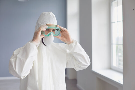 Male medicine specialist wearing PPE face mask and body protective suit putting on protection glasses