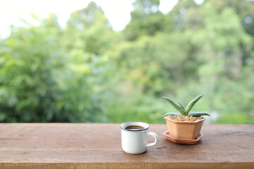 Coffee in rustic cup with aloe vera plant in brown pot on brown wooden table at outdoor