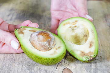 Women's hands hold Cut ugly avocado with black spots closeup
