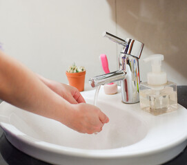 Light-skinned Asian woman rinsing hands in the bathroom sink. Shows hygiene and cleanliness for...