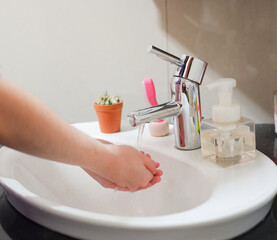 Light-skinned Asian woman rinsing hands in the bathroom sink. Shows hygiene and cleanliness for...