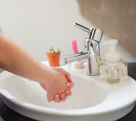 Light-skinned Asian woman rinsing hands in the bathroom sink. Shows hygiene and cleanliness for...
