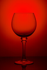 Empty glass of red wine against red background. Glass isolated on red surface. Studio shot of red wine glass silhouette.