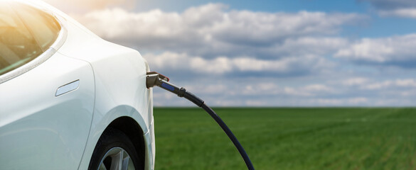 Close up of electric car with a connected charging cable on the blurred green field