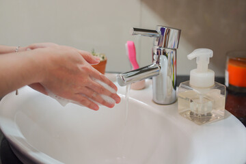 Light-skinned Asian woman washing foamy hands in the bathroom sink with soap. Shows hygiene and...