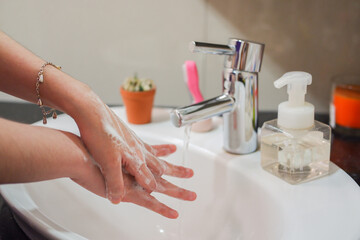 Light-skinned Asian woman washing foamy hands in the bathroom sink with soap. Shows hygiene and...