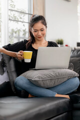 Naklejka premium Young asian woman using laptop while sitting on a couch at home.