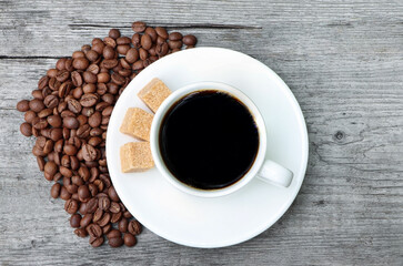 A cup of coffee with coffee beans and cane sugar on a wooden background.Heap of coffee beans. White coffee cup and saucer. Espresso coffee. Old wooden table.