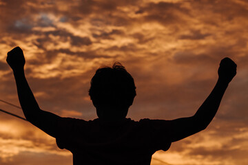 Silhouette of a kid raising his arms in front of the beautiful sunset