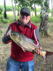 Smiling male angler showing his wife and children fish which he catched yesterday in morning on lake, having happy expression feeling pride