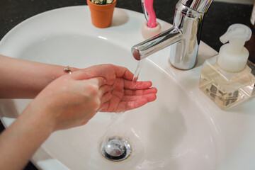 Light-skinned Asian woman rinsing hands in the bathroom sink. Shows hygiene and cleanliness for...