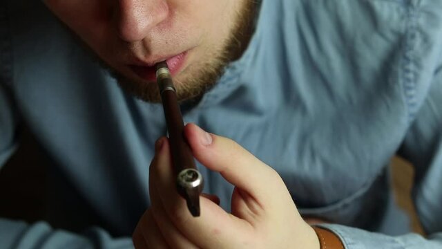 Man with a beard enjoys smoking real tobacco. Nods approvingly. Using smoking pipe
