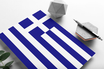 Greece flag on minimalist paper background. National invitation letter with stylish pen on stone. Communication concept.