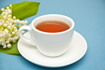 Lily of the valley flowers and cup of tea on blue background. Flat lay, top view, copy space.
