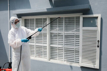 Professional cleaning staff with a To wear protective medical mask and PPE suit use chemical sprayer protect decontamination indoors. remove bacterias, viruses, and infections from the surface. COVID-