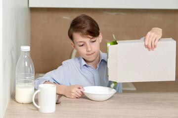 Beautiful baby boy pours cornflakes from a paper box into a white plate.