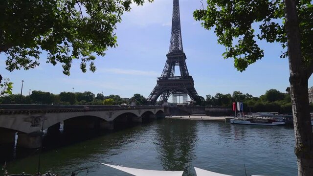 Eiffel tower, seine river and Jena bridge during sunny summer day, tilt up wide shot in the shade of the trees