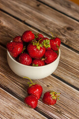 
Ripe juicy strawberries in a white round plate on a wooden table.