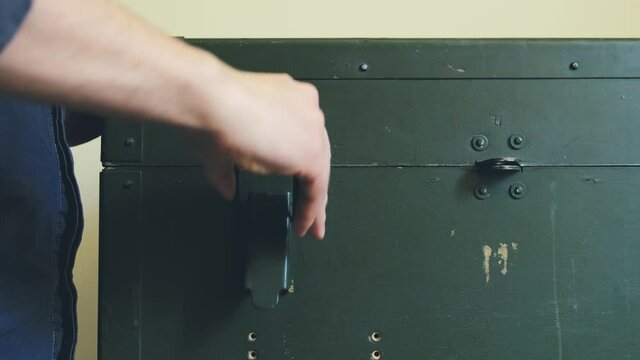 Man's Hands Open Green Military Storage Box for Ammunition. Green box from the War with Scratches and Locks in front.