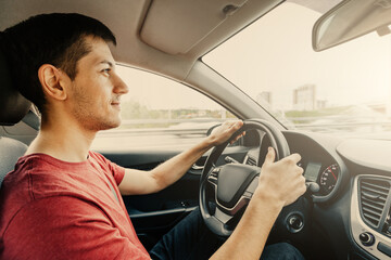 A young man in casual clothes is driving a car. Concept of a driving school student and a novice at the steering wheel