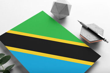 Tanzania flag on minimalist paper background. National invitation letter with stylish pen on stone. Communication concept.