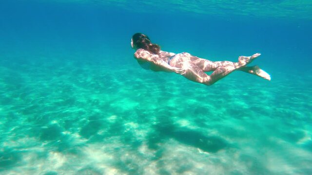 Young woman swimming underwater in the ocean alone at remote beach