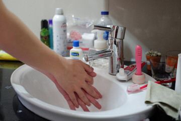 Light-skinned Asian woman rinsing hands in the bathroom sink. Shows hygiene and cleanliness for virus or bacterial spread prevention