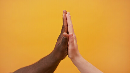 black and white hands holding together isolated on the orange background. Close up.