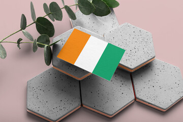 Cote D'Ivoire flag on hexagon stylish stones. Pink copy space background. Flat lay, top view...