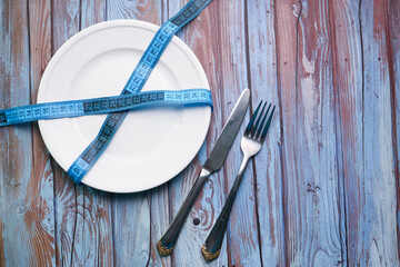 Clean plate with measurement tape and cutlery on wooden background