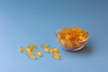 A lot of soft jelly capsules with fish oil as a source of Omega 3 in a transparent  bowl on blue...