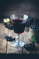 homemade black chokeberry wine or liqueur with ripe berries on wooden background