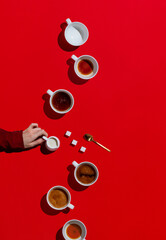 Flat lay of woman's hand holding creamer with oat milk and various cups of coffee on red