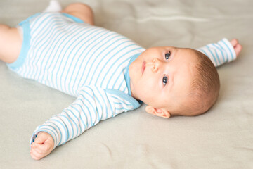 Little cute baby boy, 3 months old, lying down on gray blanket, looking up while playing and...