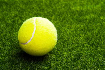 A tennis ball on a green artificial lawn with a copy of space.