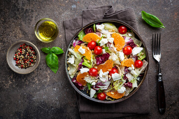 Fresh green mixed salad leaves frisee, radicchio and lamb's lettuce with tomato, olives and tangerine in a plate, top view.