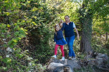 Father and daughter walking on a log in a park in summer. Copy space. Lifestyle concept.