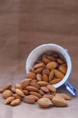 Almonds scattered from an inverted cup on a pale  brown background. Copy space. Vertical image. Selective focus.
