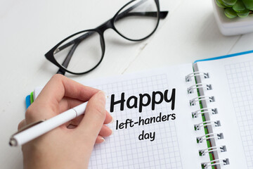 The female left hand writes with a pen in a notebook congratulations on the day of the lefthander