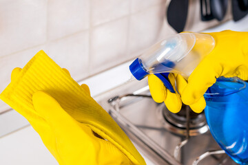 Cropped shot of a woman wearing rubber gloves  cleaning the kitchen counter with disinfectant spray. Covid-19 prevention and hygiene concept.