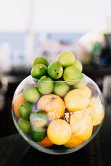 Transparent round vase with lemons, oranges and limes. Bright summer colors, fruits for a cocktail or fresh.