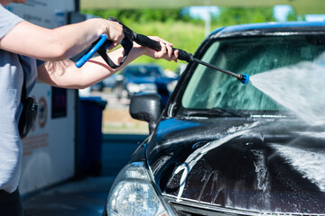 the driver washes his car in a self-service car wash. foam on the car. clean car. car wash process