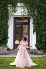 Beautiful woman in flying airy pink dress on background of door overgrown with wild grapes. Pretty young caucasian girl plays with her dress. Girl dance in flowing dress