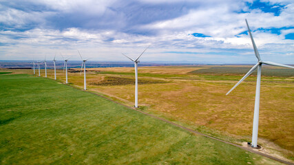 Fototapeta na wymiar Wind farm with turbines lined up in a row with farm fields